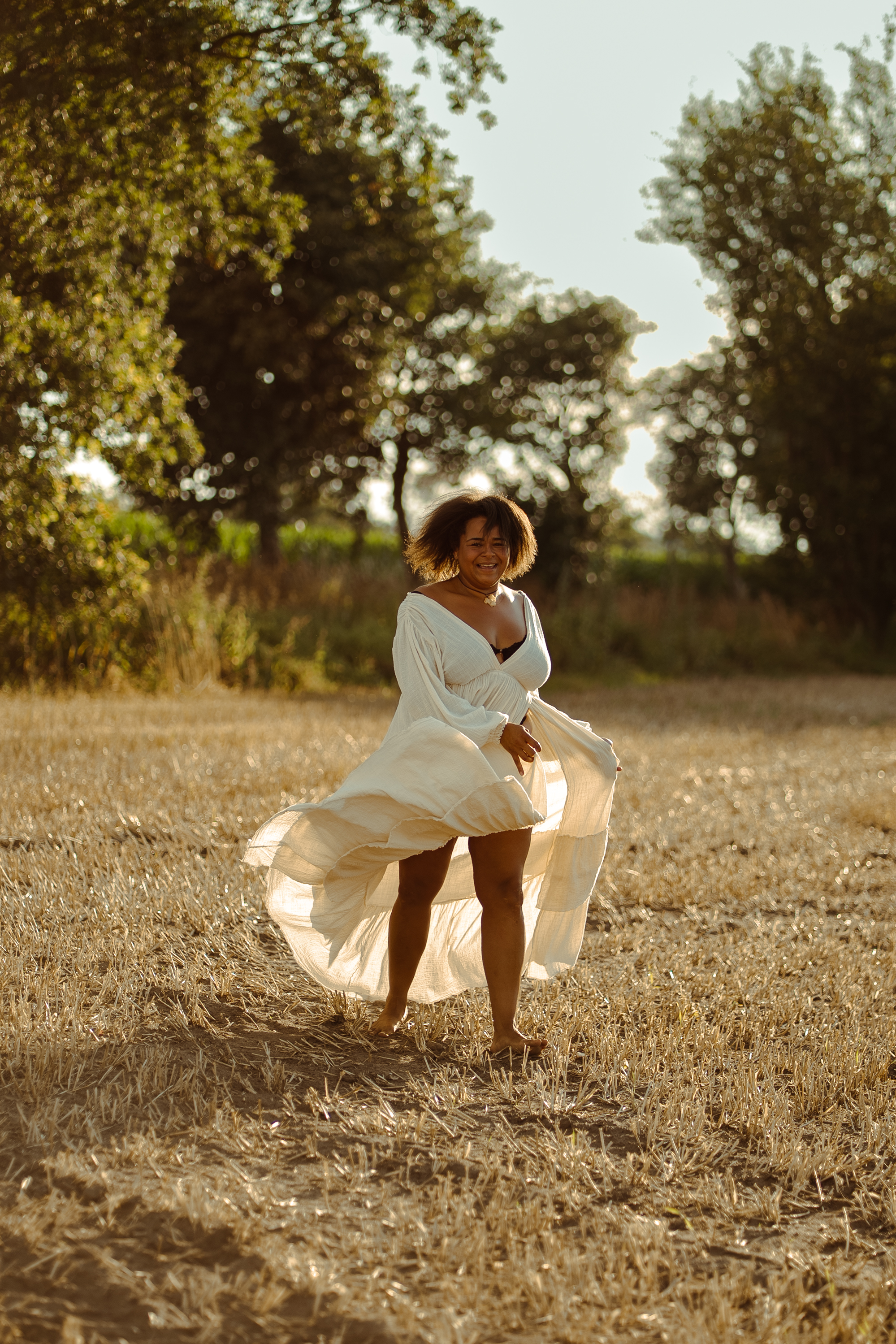 Natürliche Frauenfotografie Koblenz – Frau tanzt im weißen Kleid auf einem Feld im Sonnenuntergang